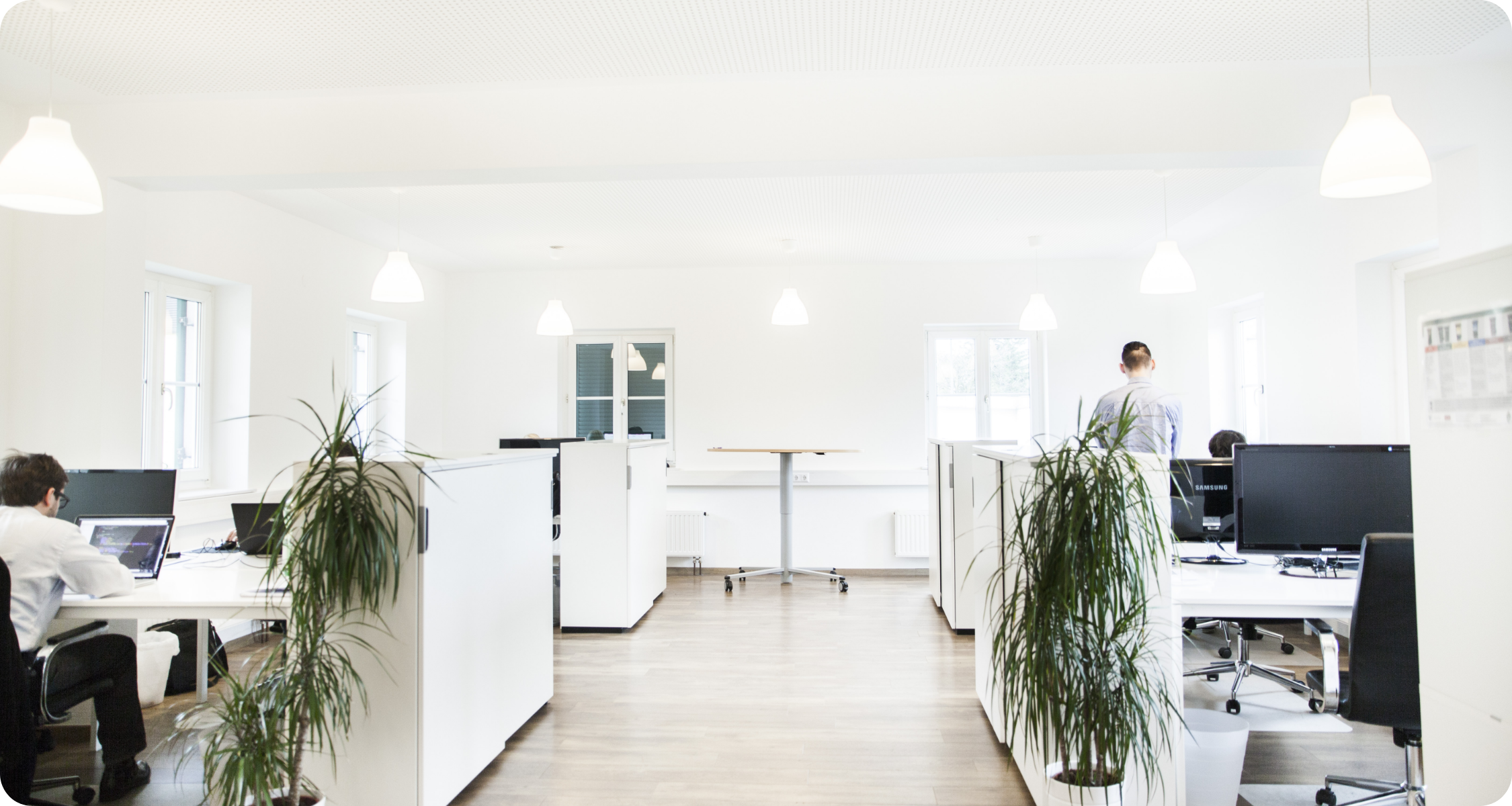 Ein Raum mit mehreren Arbeitsplätzen und Mitarbeitern, die am Laptop arbeiten.