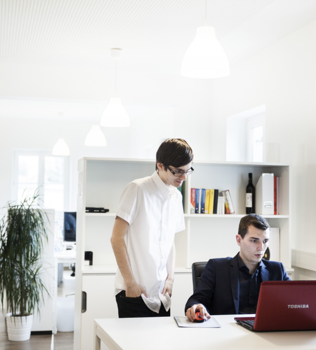 Ein Mitarbeiter am Laptop und ein weiterer Mitarbeiter, der danebensteht.